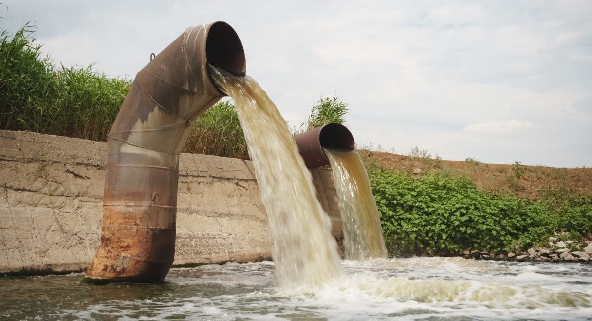 Wastewater from two large rusty pipes merge into the river in clouds of steam