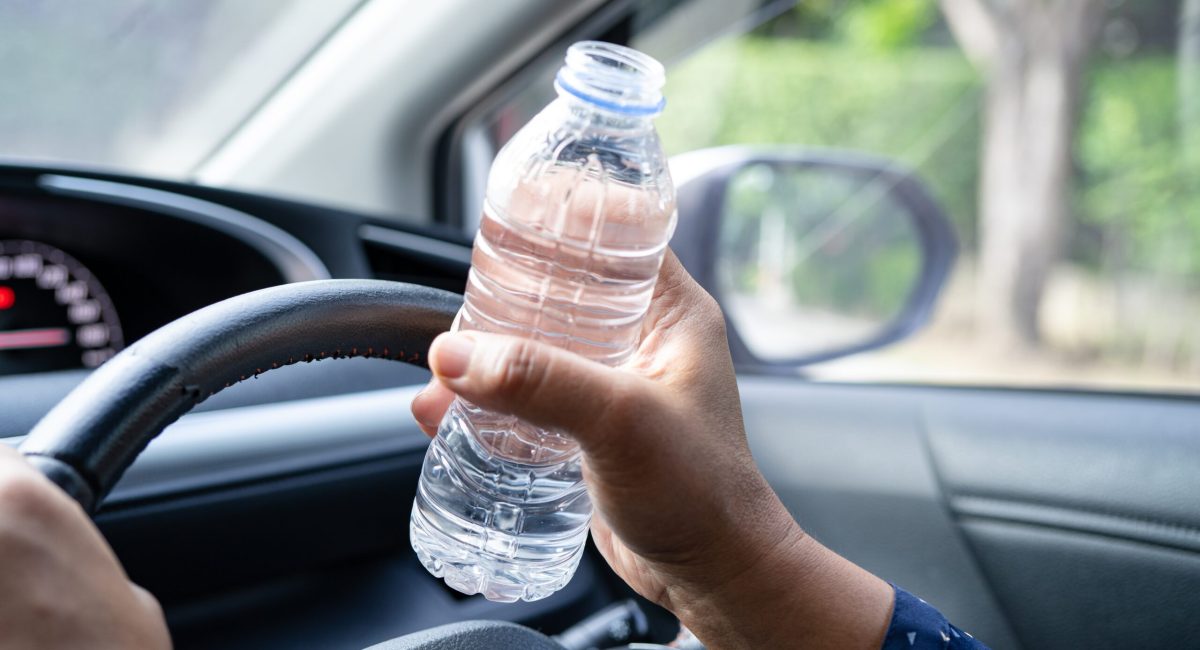 Asian woman driver holding bottle for drink water while driving a car. Plastic hot water bottle cause fire.