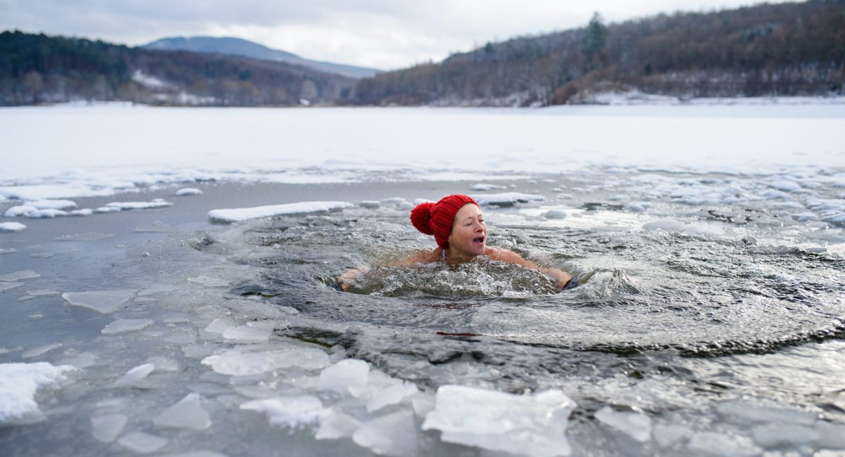 A front view of active senior woman in swimsuit outdoors in water in winter, cold therapy concept.